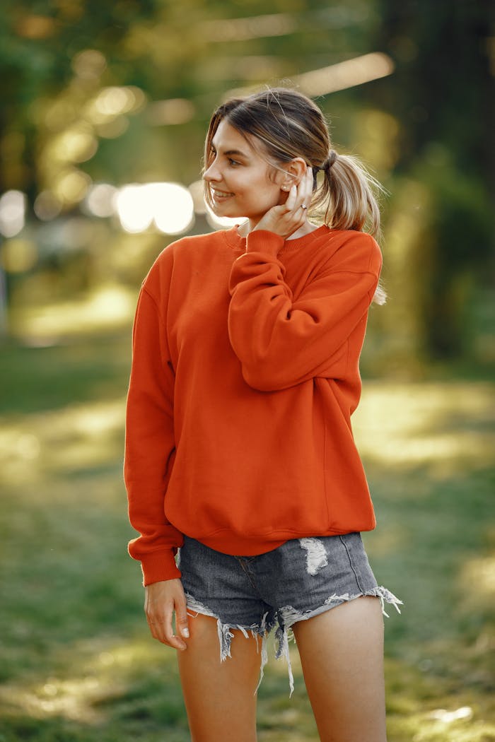 about-us Cheerful young woman in red sweatshirt and denim shorts enjoying a sunny day outdoors.